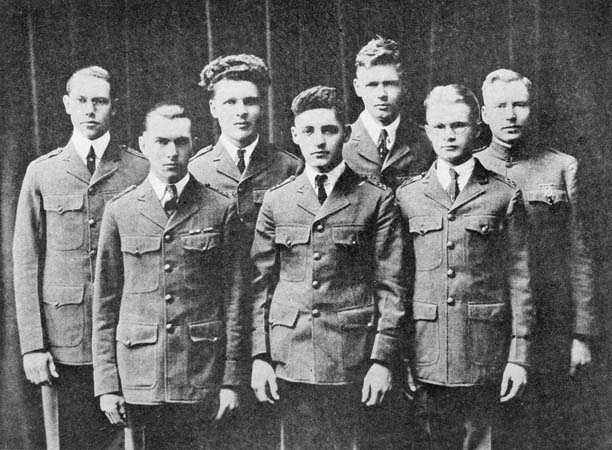 Seven men stand together in military school uniforms.